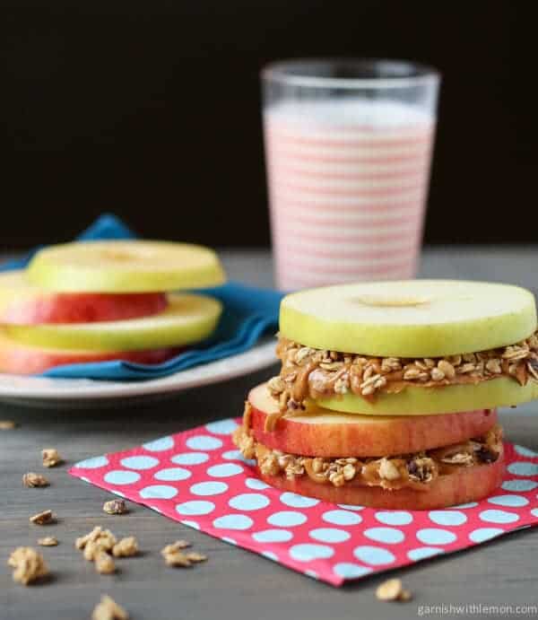 Stack of Apple Sandwiches with Almond Butter and Granola. Glass of milk in background.