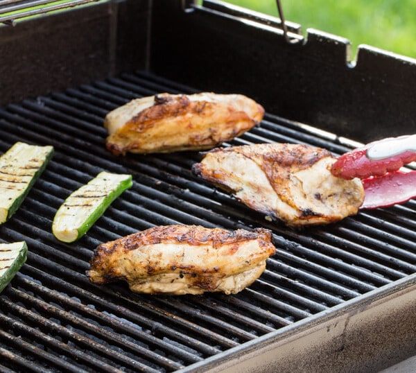 A grill that has chicken breasts  and zucchini cooking on it.