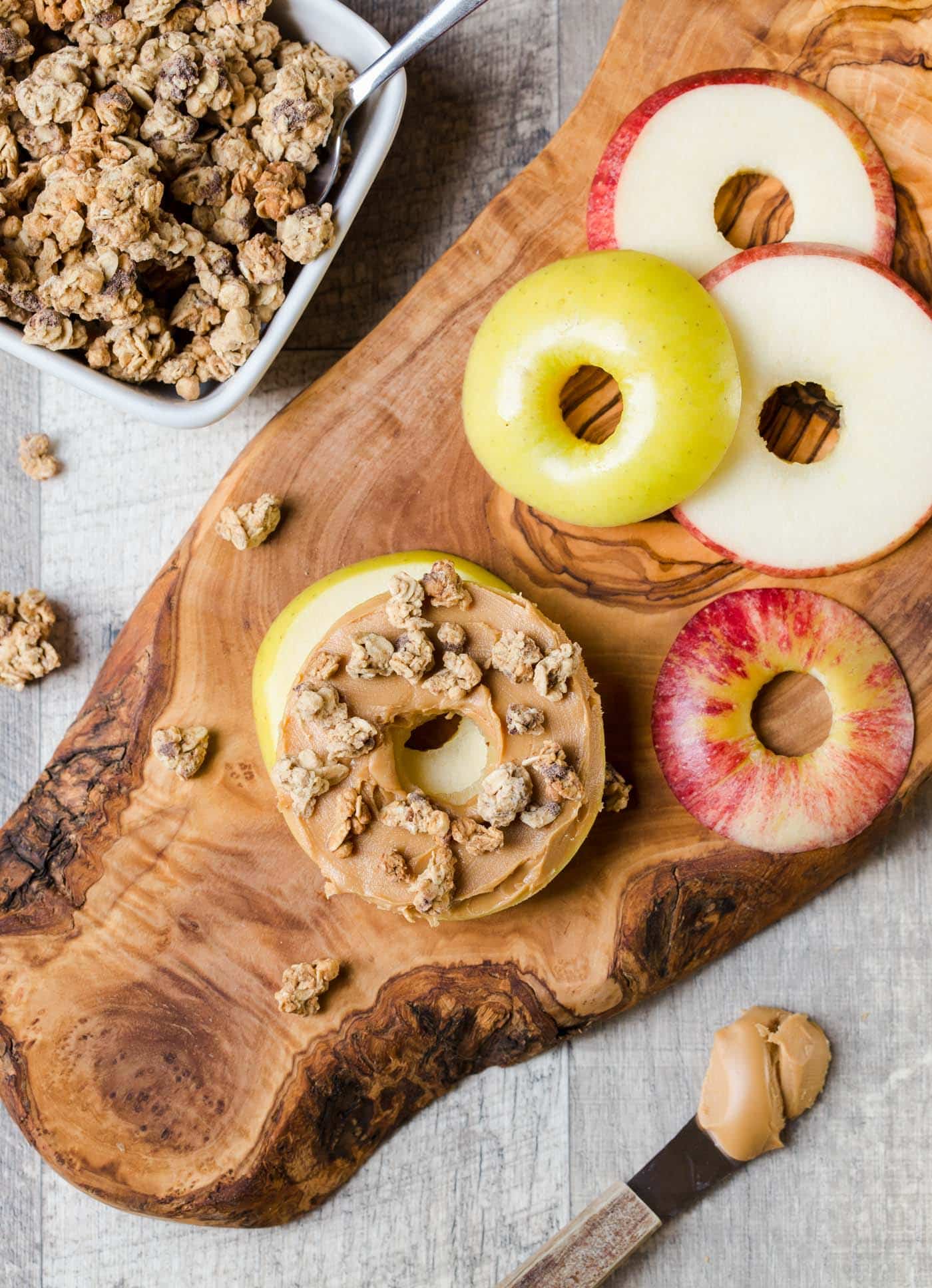apple slices on wooden board with almond butter and granola.