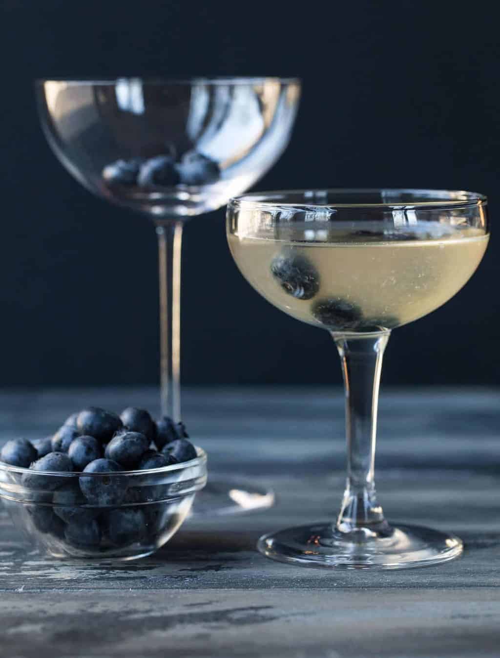 Martini is a coupe glass with blueberry floating in it for garnish.