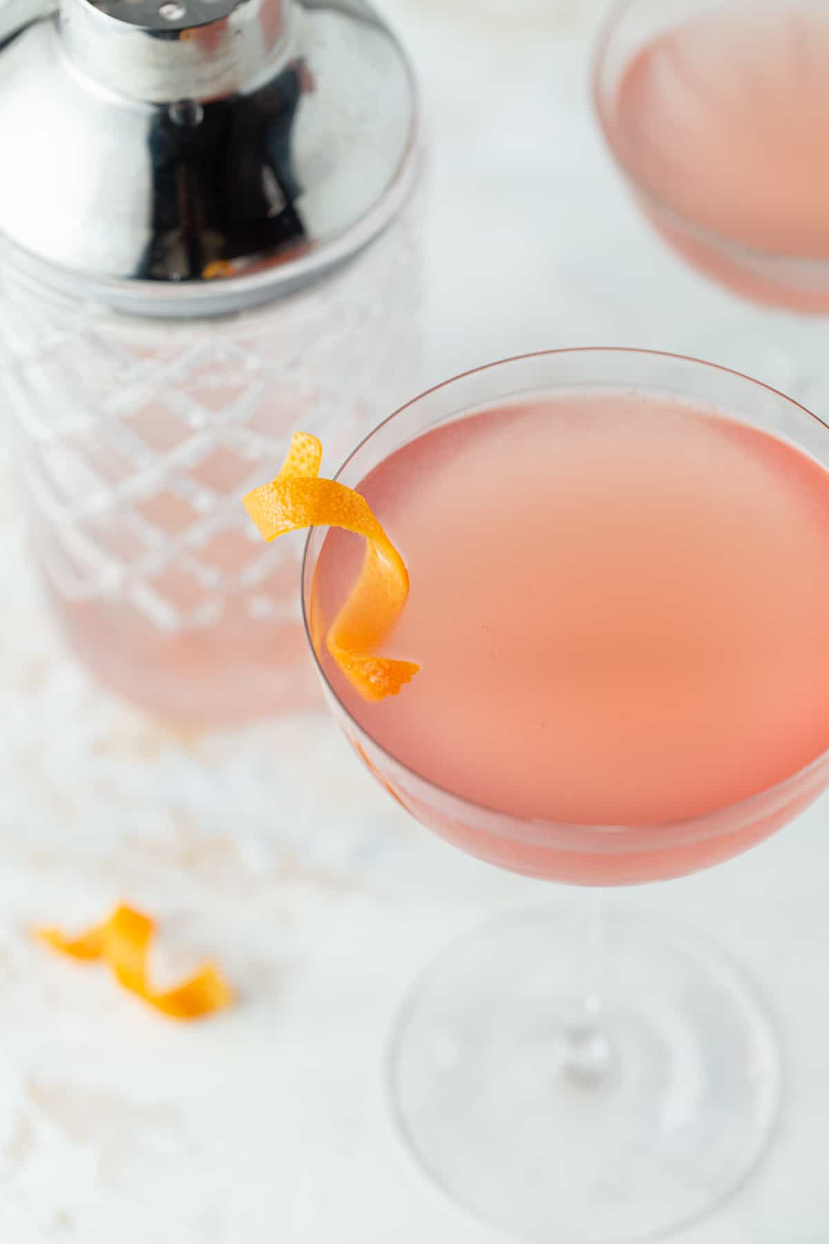 Close up of pink grapefruit martini in a tall coupe glass with an orange peel for a garnish.